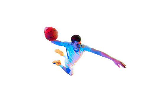Action shot from above of player performing powerful basketball dunk against white studio background in neon light. Concept of professional sport, energy, strength and power, match, tournament.