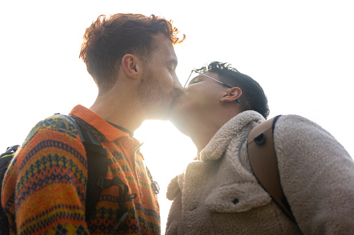 Two men on their first date together, enjoying the day out in Newcastle upon Tyne, England. They are kissing each other as the sun shines through between their bodies.