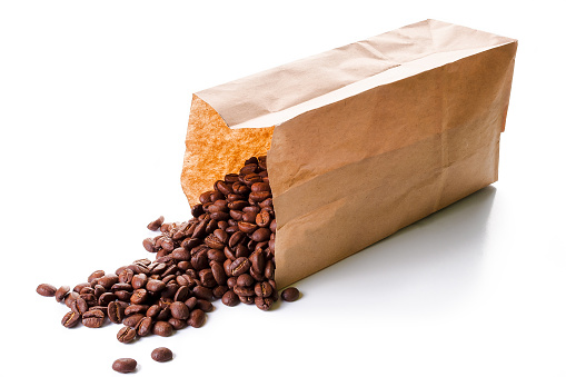 roasted coffee beans spilled in front of a brown disposable package made from kraft paper on the white background. recyclable and sustainable mockup concept for eco friendly branding