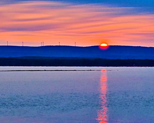 The sun rising over the mountain meeting a row of wind turbine