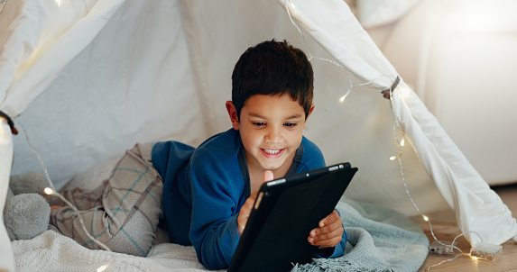 Tablet, relax and boy child in a tent playing an online game on the internet in the living room. Happy, entertainment and kid watching a movie, video or show on a digital technology in a blanket fort