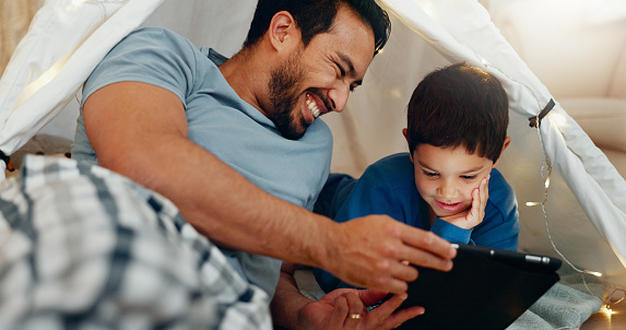 Bonding, tablet and father in a tent with kid watching a movie, video or show online. Happy, smile and young dad networking on social media with boy kid on digital technology in blanket fort at home.