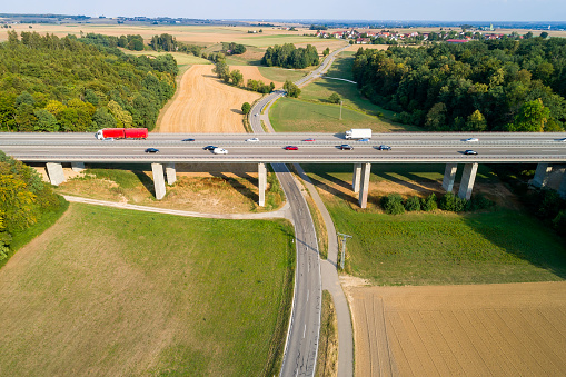 Aerial view of a highway bridge with traffic of cars and trucks, surrounded by forests and fields at sunset in summer.