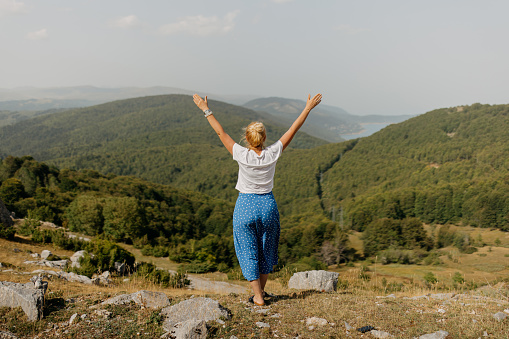 A mature woman, aged 40-44, immerses herself in a sustainable and healthy lifestyle amidst the stunning autumn mountain landscape. With arms outstretched and eyes closed, she practices relaxation and breathing exercises, finding motivation and tranquility in the crisp mountain air