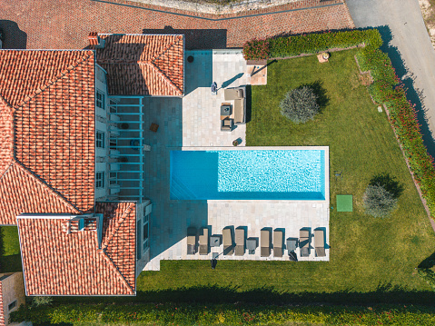 Bird's eye view of an elegantly renovated luxury  hotel with a big swimming pool, several sunbeds and huge lawn around the patio. Private and secluded with a green hedge.