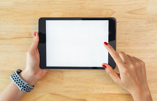 Hands holding digital tablet with mockup of blank screen on desk in office room.
