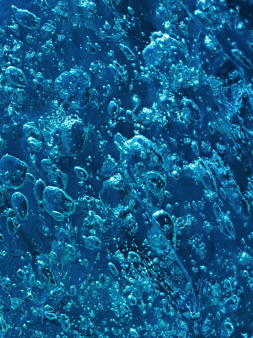Vivid blue ice texture with intricate bubbles, illuminated by light.