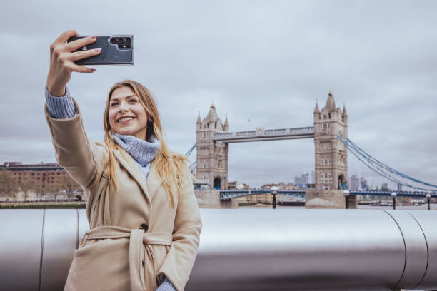 istock Young beutiful blond woman in her 30s smiling while taking selfie with her smart mobile phone device in down town in front of Tower Bridge, City of London, England - creative stock photo 2030042552