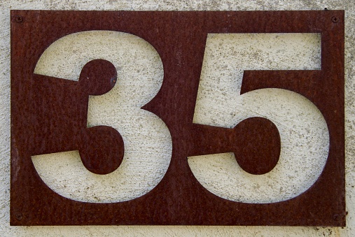 A brown metal house number plate mounted on concrete showing the number 35