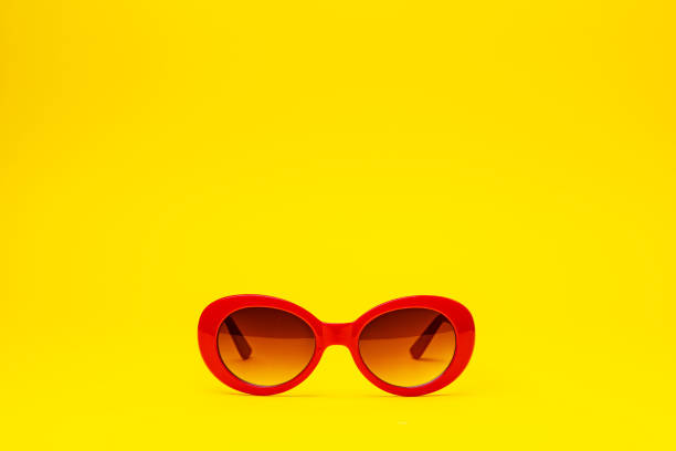 A pair of red sunglasses with tinted lenses on a yellow backdrop.
