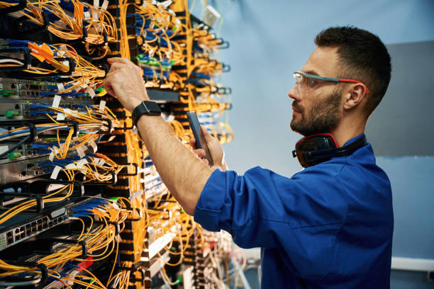 istock Side view. Young man is working with internet equipment and wires in server room 2030097456