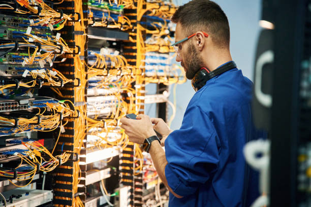 Holding smartphone. Young man is working with internet equipment and wires in server room Holding smartphone. Young man is working with internet equipment and wires in server room. computer cable stock pictures, royalty-free photos & images