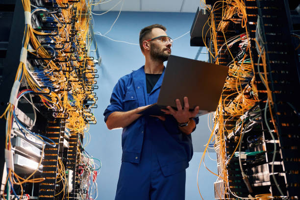istock Holding laptop. Young man is working with internet equipment and wires in server room 2030099587