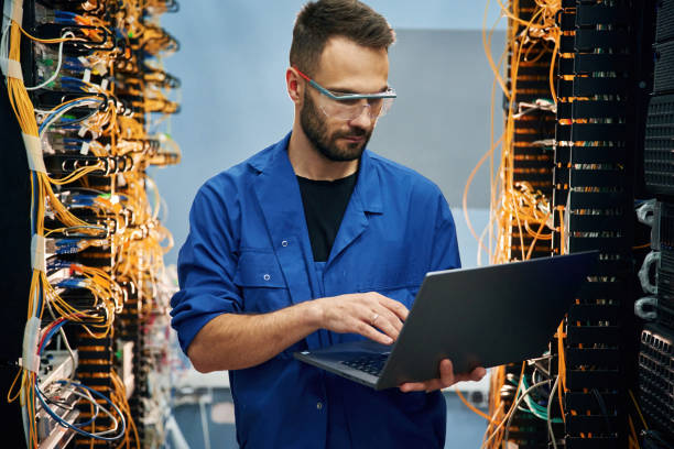istock Holding laptop. Young man is working with internet equipment and wires in server room 2030100131