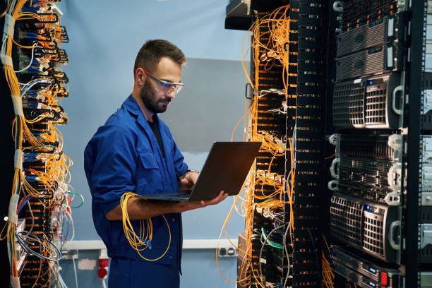 istock With laptop in hands. Young man is working with internet equipment and wires in server room 2030101219