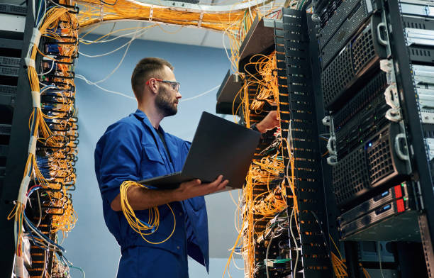 istock With laptop in hands. Young man is working with internet equipment and wires in server room 2030101228