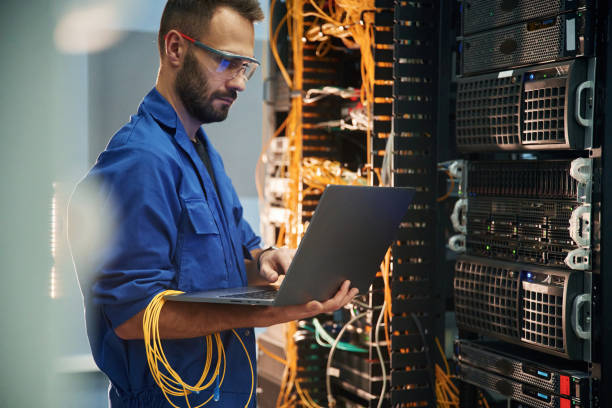 istock Silver colored laptop in hands. Young man is working with internet equipment and wires in server room 2030101962