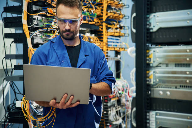 istock Silver colored laptop in hands. Young man is working with internet equipment and wires in server room 2030102739