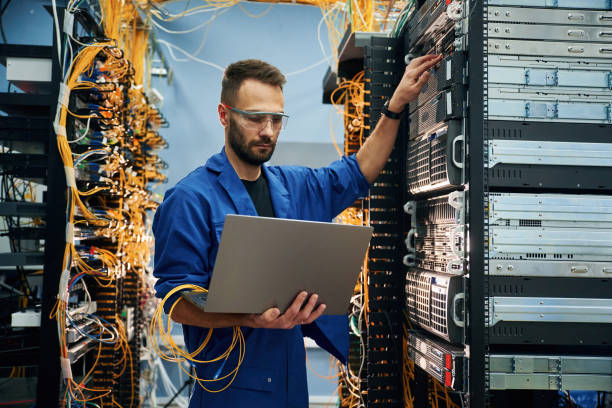 istock Using the laptop. Young man is working with internet equipment and wires in server room 2030102866