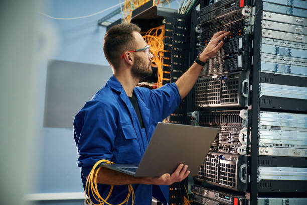 istock Using the laptop. Young man is working with internet equipment and wires in server room 2030102876