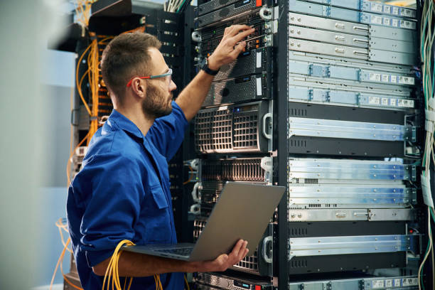 Using the laptop. Young man is working with internet equipment and wires in server room