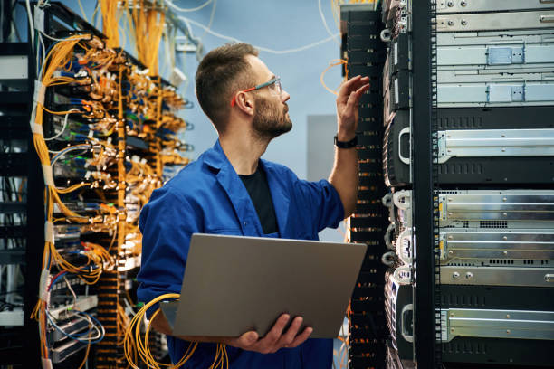 istock Young man is working with internet equipment and wires in server room 2030103943
