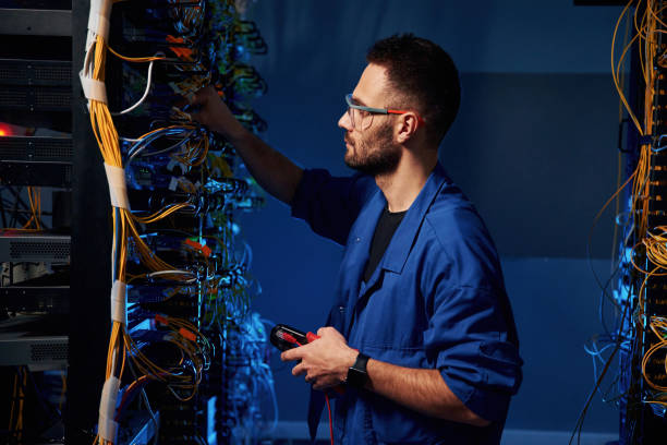 istock Blue colored lighting. Young man is working with internet equipment and wires in server room 2030111375