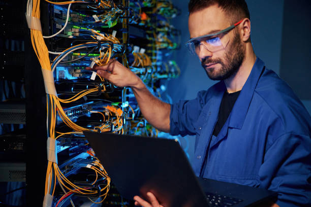 istock Cables management. Young man is working with internet equipment and wires in server room 2030113019