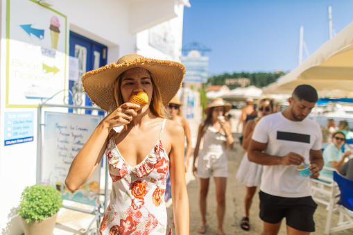 Group of gorgeous young women and men have a fun at summer in the beautiful village Fiscardo on Kefalonia island in Greece. They are walking on streets and eating ice-cream. Beautiful young people are friends. They traveling together and looks very happy