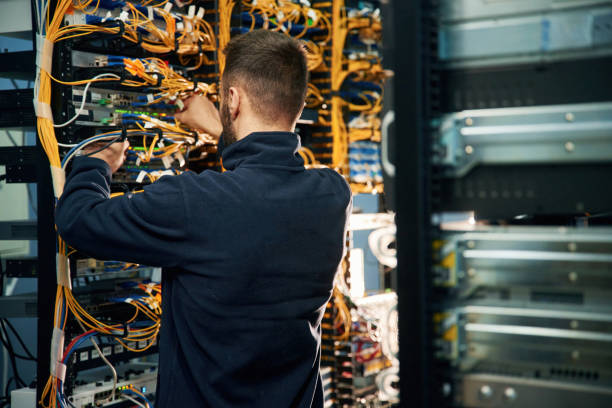 istock Young man is working with internet equipment and wires in server room 2030115718