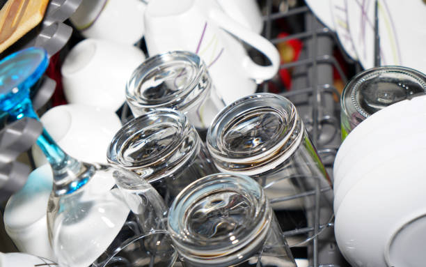 Close up of Asian senior woman's hand putting dirty glass cup in dishwasher.