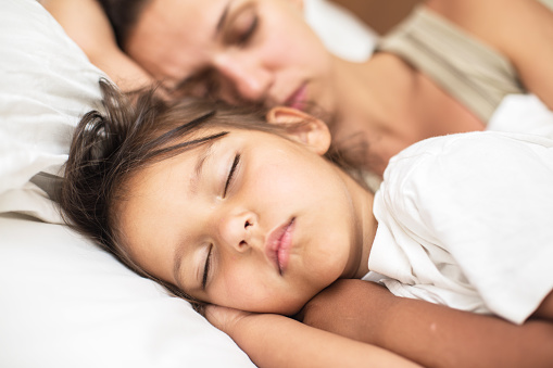 Sleeping kid girl and her mother in the bed.