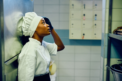 African American female cook feeling exhausted while working in a restaurant kitchen. Copy space.