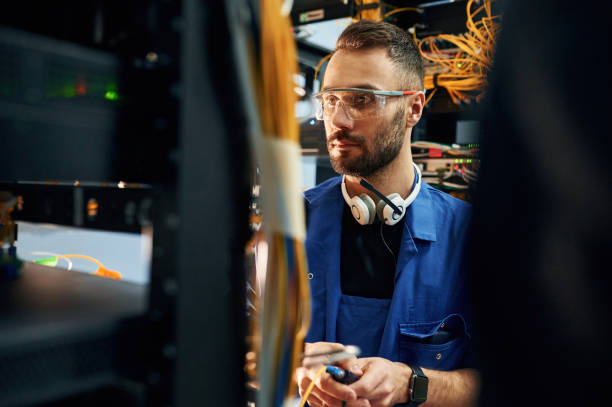 istock In blue colored uniform. Young man is working with internet equipment and wires in server room 2030124010