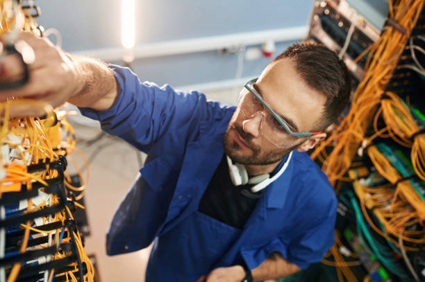 istock In blue colored uniform. Young man is working with internet equipment and wires in server room 2030124853