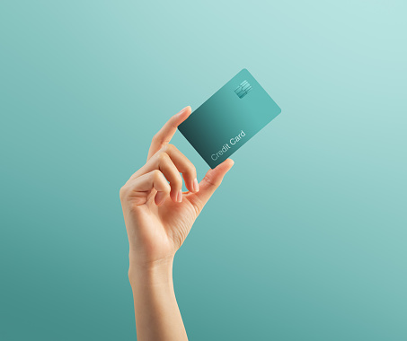 Hand holding credit card on turquoise background.