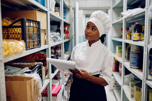 African American female cook checking kitchen's supplies while working in a restaurant.