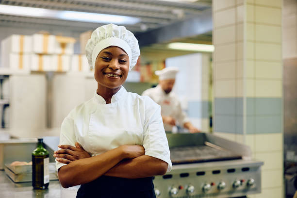 istock Happy black cook standing with her arms crossed while working in a restaurant and looking at camera. 2030128047
