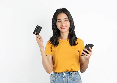 Happy young Asian woman holding smartphone with credit card on white background.