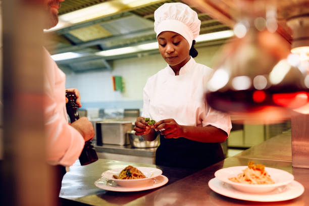 istock Black cook and her coworker decorating a dish while preparing food in a restaurant. 2030131291