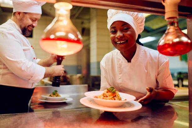 istock Happy black female chef serving a dish in restaurant kitchen and looking at camera. 2030131320