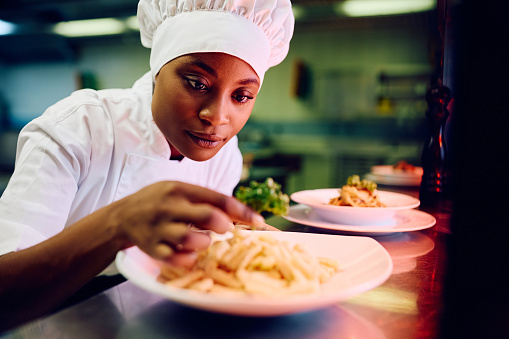 African American female chef decorating food plate cooking in the kitchen.