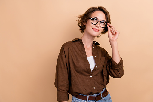 Portrait of gorgeous clever girl with bob hairstyle wear stylish shirt touch eyewear look empty space isolated on beige color background.