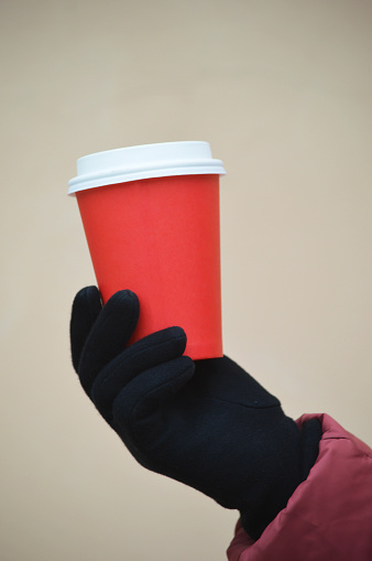 Red paper disposable cup for tea or coffee in a woman's hand. Mockup. Place for logo.