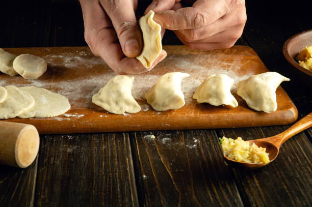istock The chef is making dumplings with his hands. Step-by-step process of preparing homemade dumplings filled with mashed potatoes on a dark table. Ukrainian cuisine. Close-up view. 2030159789