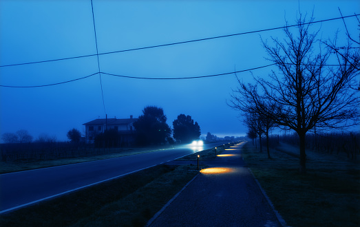 One car drives in the countryside at dawn, in low light, alongside  a bike lane