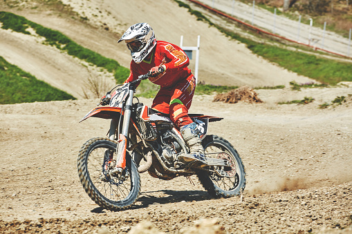 Rear view of dirt bike race riding fast on off-road dirt track.