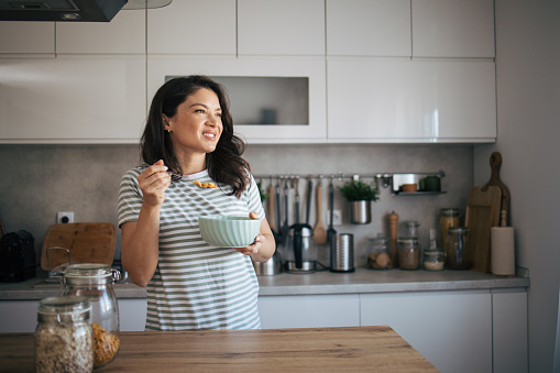 beautiful happy adult woman eating breakfast in the kitchen and looking at the window.