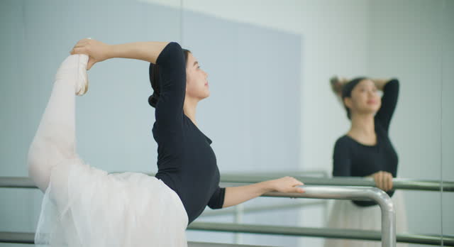 Ballerina girl stretching practicing near ballet barre in dance studio.