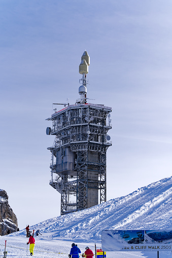 Concrete and metal communications tower on top of Titlis mountain with skiers on a sunny winter day with mountain panorama. Photo taken February 21st, 2024, Titlis, Engelberg, Switzerland.